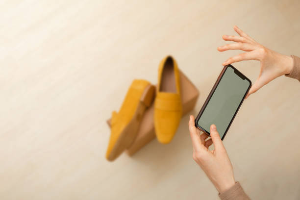 Select focus of one woman's hand with smartphone is pointing to clear screen, shooting box with suede loafers. Concept of thrift stores, resale, second hand, resale application. seleccione el enfoque de la mano de una mujer con el teléfono inteligente está apuntando a la pantalla transparente, cuadro de disparo con mocasines de gamuza. concepto de tiendas de segunda mano, reventa, segunda mano, aplicación de reventa.