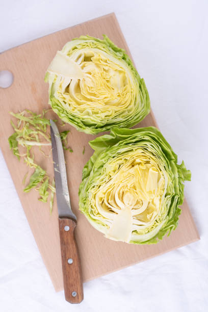 Fresh early cabbage cut into halves on a cutting board with a knife on a white background, close up.