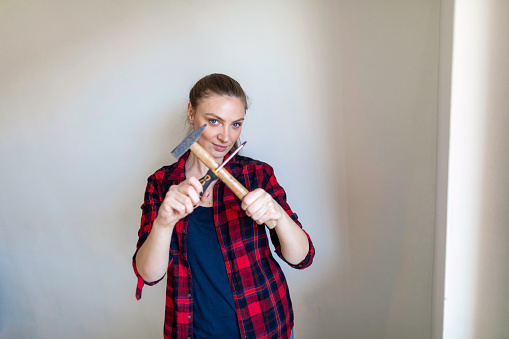 Portrait of young woman holding hammer and screwdriver at home