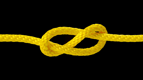 Close-up of yellow rope being pulled into tight knot against black background.