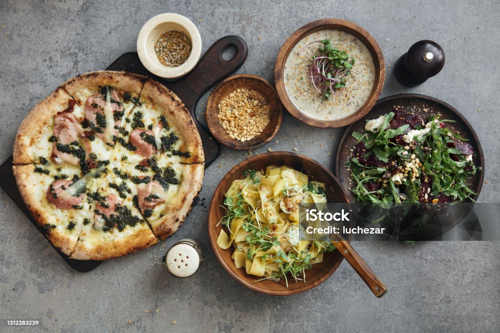 Italian Dishes Zucchini and lemon pappardelle with peanuts. Beet salad with arugula and feta. Italian pizza with mortadella. Flat lay top-down composition on concrete background. Pizza Stock Photo