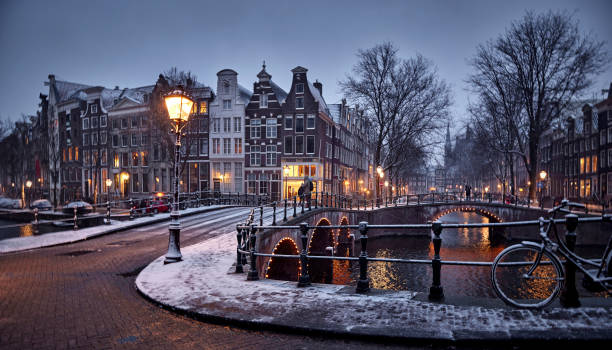 Amsterdam in snow Amsterdam canals and typical canal houses in the old part of the city during a night in winter. The streets are covered in white from the snow, the city lights are on and the sky is grey because of the clouds. You can see some snow falling down. dutch culture photos stock pictures, royalty-free photos & images