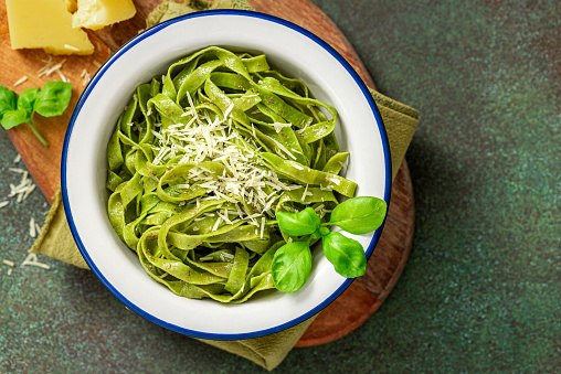 Spinach pasta with pesto sauce and grated cheese in a white plate on a dark background top view. Italian food, Mediterranean cuisine. Green pasta with pesto and parmesan. Copy space for text