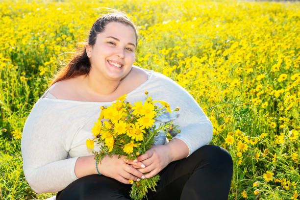beautiful plus-size girl poses outdoors with a bouquet of daisies stock photo