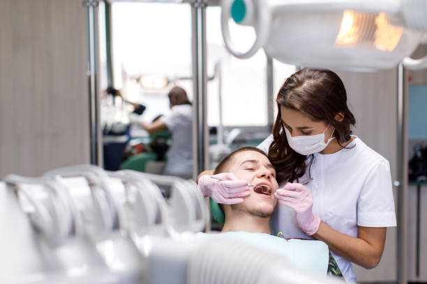 병원에서 중간 성인 남자에 의해 서 젊은 여성 치과 의사의 초상화. 치과 진료에서 환자 치아를 수리하는 여성 치과 의사 - ambulant patient 뉴스 사진 이미지