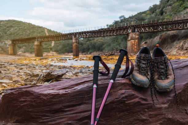 scarponi da trekking e bastoncini da trekking su una pietra focalizzata e sullo sfondo un vecchio ponte di ferro sul rio tinto. - at the bottom of boot sole of shoe shoe foto e immagini stock