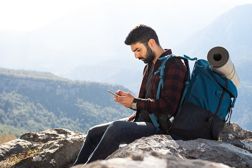 Young hiker using mobile phone while resting on the top of a mountain.