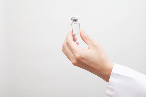 A glass bottle of vaccine in the palm of a doctor