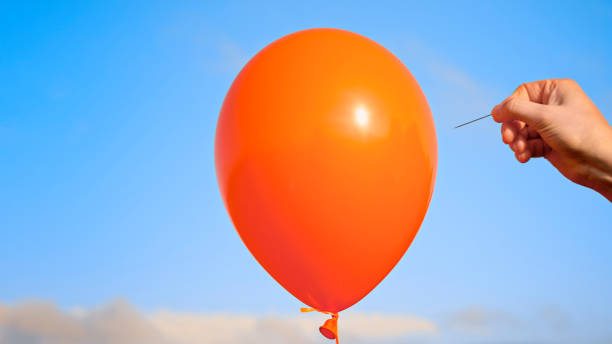 istock Man popping orange balloon with pin 1312302365