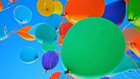 Group of colourful balloons flying away in blue sky.