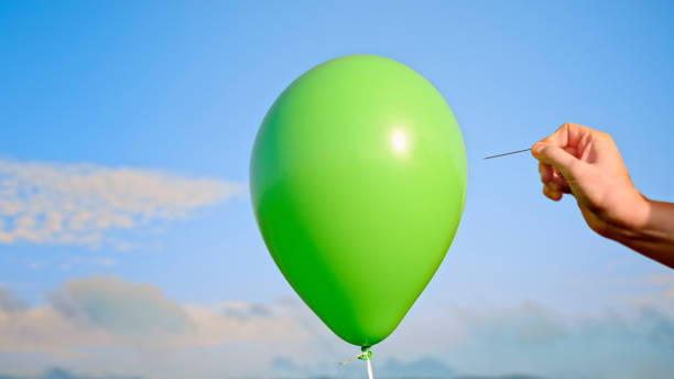 istock Man popping green balloon with pin 1312302384