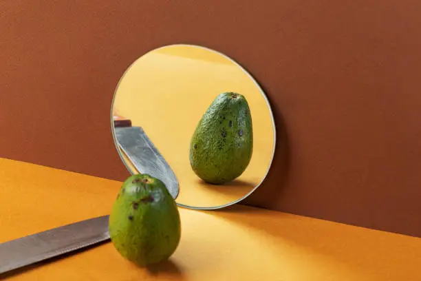 Fresh avocados and kitchen knife in mirror reflection