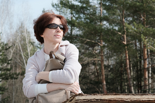Mature woman is sitting on bench in sunny forest