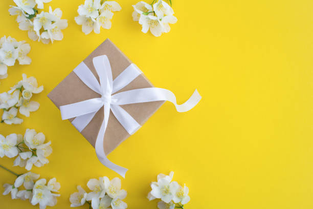 istock Gift with white bow and jasmine flowers on the yellow background.Top view.Copy space. 1312304047