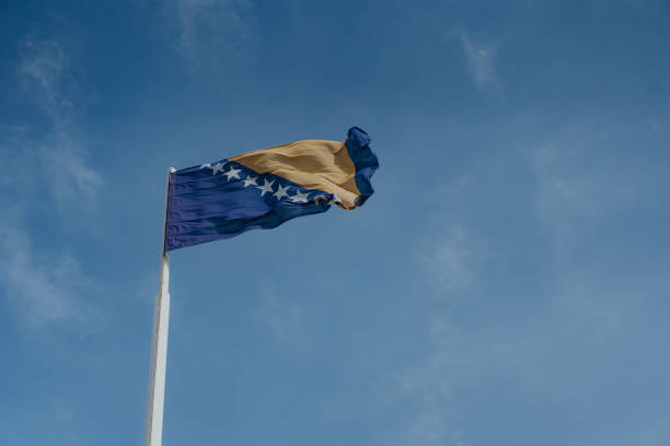 bandiera nazionale della bosnia-erzegovina su un cielo blu nuvoloso durante una giornata di sole - bosnia herzegovinan flag foto e immagini stock