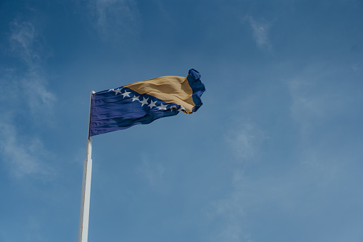 National flag of Bosnia and Herzegovina on a cloudy blue sky in during a sunny day