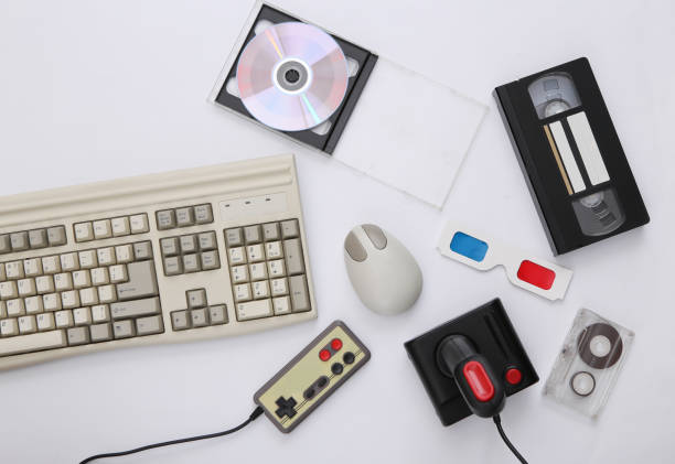 Flat lay 80s attribute composition. PC keyboard, mouse, gamepads, audio and video tapes, CD, 3D glasses. Retro Electronics, gadgets and devices. Entertainment and gaming. White background. Top view