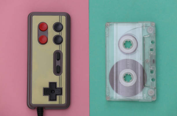 istock Wired retro gamepad and audio cassette on pink blue background. Retro Attributes. Top view 1312310655