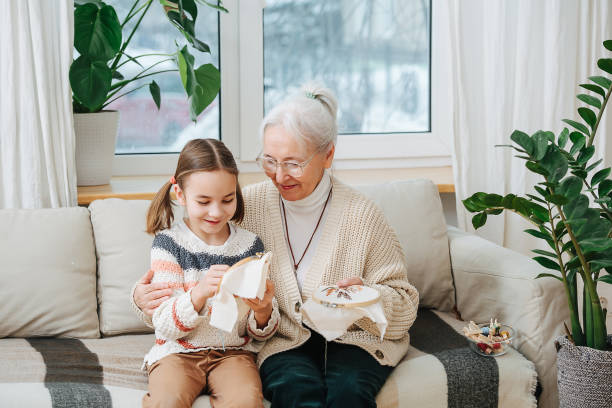 할머니는 자수 그녀의 손녀를 가르친다, 그들은 집에서 소파에 앉아 - embroider embroidery caucasian skill 뉴스 사진 이미지