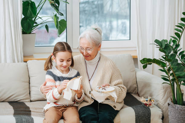 grandmother teaches her granddaughter to embroider, they sit on the sofa at home - embroider imagens e fotografias de stock