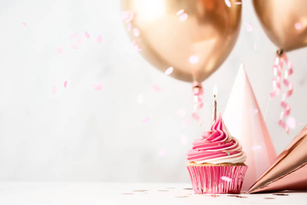 Birthday celebration with cupcake and balloons Birthday celebration with pink birthday cupcake, party hats and rose gold balloons streamer photos stock pictures, royalty-free photos & images