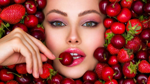 Attractive woman tasting cherry and strawberry. Beautiful woman with fashion makeup and a vivid background. Young girl with bright makeup and a berry background. Beautiful caucasian woman biting a berry. Attractive woman tasting cherry. Beautiful woman with fashion makeup and a vivid background. tasting cherry eating human face stock pictures, royalty-free photos & images