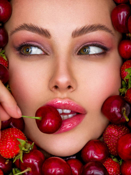 Attractive woman tasting cherry and strawberry. Beautiful woman with fashion makeup and a vivid background. Young girl with bright makeup and a berry background. Beautiful caucasian woman biting a berry. Attractive woman tasting cherry. Beautiful woman with fashion makeup and a vivid background. tasting cherry eating human face stock pictures, royalty-free photos & images