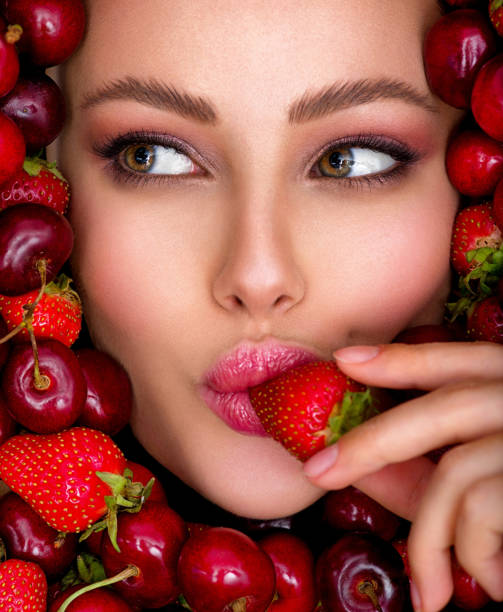 Attractive woman tasting cherry and strawberry. Beautiful woman with fashion makeup and a vivid background. Young girl with bright makeup and a berry background. Beautiful caucasian woman biting a berry. Attractive woman tasting cherry and strawberry. Beautiful woman with fashion makeup and a vivid background. tasting cherry eating human face stock pictures, royalty-free photos & images