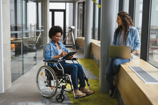 Disabled computer programmer discussing with female coworker in office hallway