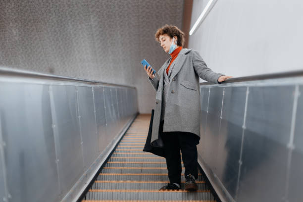 femme avec un smartphone restant sur les étapes d’escalator et regardant en arrière - railroad station escalator staircase steps photos et images de collection