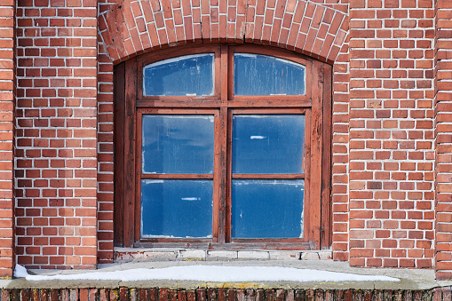One arched glass window on old red brick wall. Vintage window in brown wooden frame on red brick wall of industrial building.