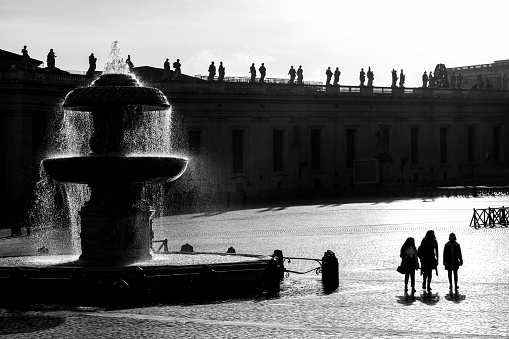 Vatican City, January 30 -- Sunlight passes through one of Bernini's fountains in the square of St. Peter's Basilica, creating a backlit effect and a suggestive atmosphere among the splashes and drops of water and some persons in back lite. In the background the silhouette of the statues of Bernini's colonnade. Image in High Definition format