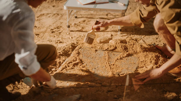 istock Archaeological Digging Site: Two Great Archeologists Work on Excavation Site, Carefully Cleaning, Lifting Newly Discovered Ancient Civilization Cultural Artifact, Historic Clay Tablet. Focus on Hands 1312318072