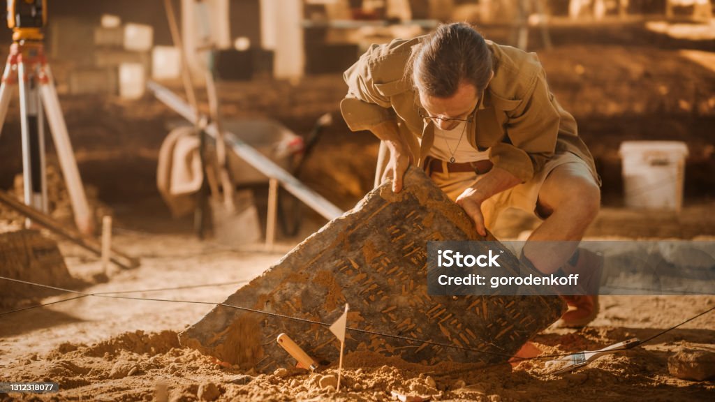 Archaeological Digging Site: Great Male Archeologist Work on Excavation Site, Carefully Cleaning, Lifting Newly Discovered Ancient Civilization Cultural Artifact, Historic Clay Tablet, Fossil Remains Mesopotamian Stock Photo