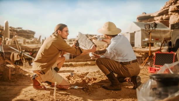 istock Archeological Digging Site: Two Great Archeologists Work on Excavation Site, Carefully Holding Newly Discovered Ancient Civilization Cultural Artifact, Historical Clay Tablet, Fossil Remains 1312318081