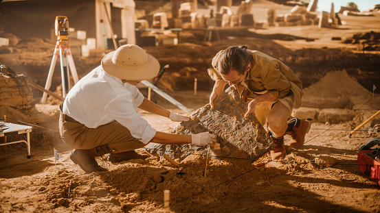 Sitio de excavación arqueológica: Dos grandes arqueólogos trabajan en el sitio de excavación, limpiando cuidadosamente, levantando artefacto cultural de la antigua civilización recién descubierto, tableta histórica de arcilla, restos fósiles photo