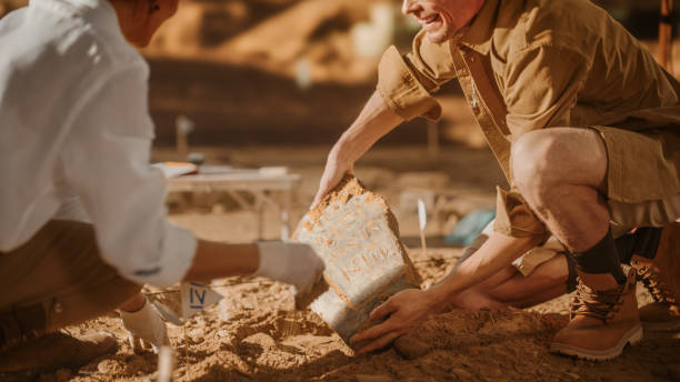 istock Archeological Digging Site: Two Great Archeologists Work on Excavation Site, Carefully Cleaning, Holding Newly Discovered Ancient Civilization Cultural Artifact, Historic Clay Tablet, Fossil Remains 1312318134