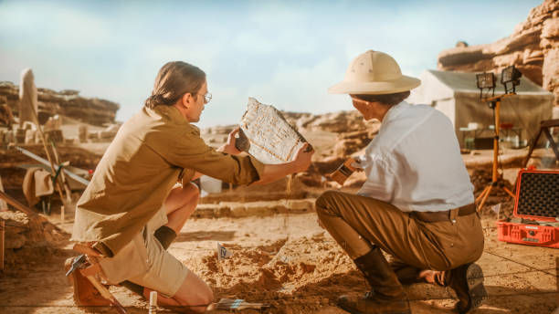 istock Archeological Digging Site: Two Great Archeologists Work on Excavation Site, Carefully Holding Newly Discovered Ancient Civilization Cultural Artifact, Historical Clay Tablet, Fossil Remains 1312318666