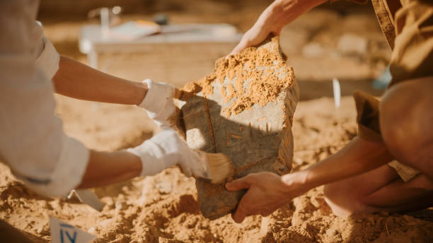 istock Archeological Digging Site: Two Great Archeologists Work on Excavation Site, Carefully Cleaning, Holding Newly Discovered Ancient Civilization Cultural Artifact, Historic Clay Tablet, Fossil Remains 1312320744