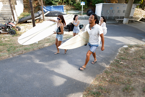 Three cheerful young surfers with surfboards walking and talking along the beach
