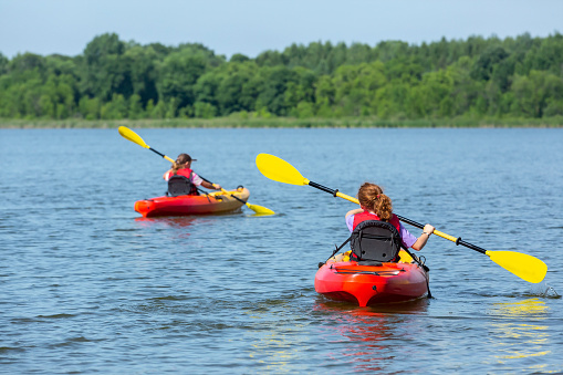 Rear view of two young girls (sisters) kayaking on a lake on a beautiful summer day.