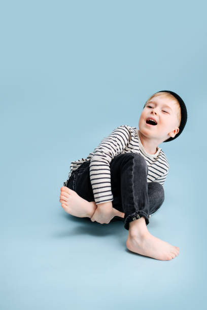 istock Acting blond boy sitting on the floor, tilting to the side, holding his leg 1312326708