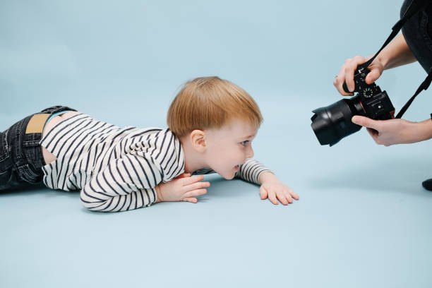 istock Cameraman capturing grinning little blond boy lying on the floor. Studio shot. 1312326718