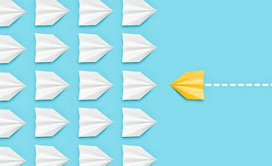 Change concepts with yellow paper boat leaving a dotted line on blue background leading among white airplane group stock photo