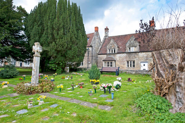 Church graveyard and cottages, Tisbury, Wiltshire, England. Ancient and medieval stone cottage architecture seen across a grassy graveyard on a bright sunny April day with blue sky and fluffy cumulus clouds in Tisbury, Wiltshire, England