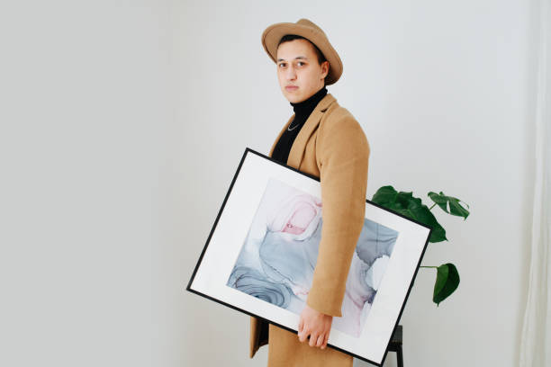 istock Stylish man in a beige suit and classical hat posing with painting under his arm 1312335123