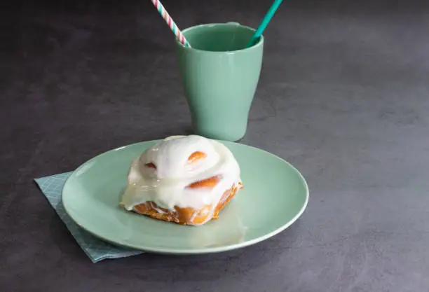 a cinnamon-sugar spiral bun with cream on a green plate with a cup of the same color on a dark background