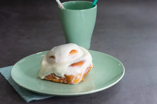 a delicious cinnamon-sugar swirl bun with cream on a green plate and a green cup on a dark background