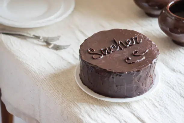 Sachertorte a chocolate gateau with apricot jam filling and chocolate icing on white plate on light linen background. Selective focus