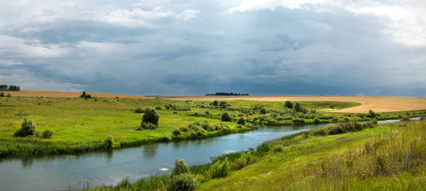 istock Summer panoramic landscape with dark stormy clouds over the calm river and green meadows. 1312338436